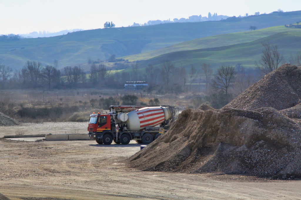 Camion betoniera vicino a cumuli di terra, paesaggio collinare.