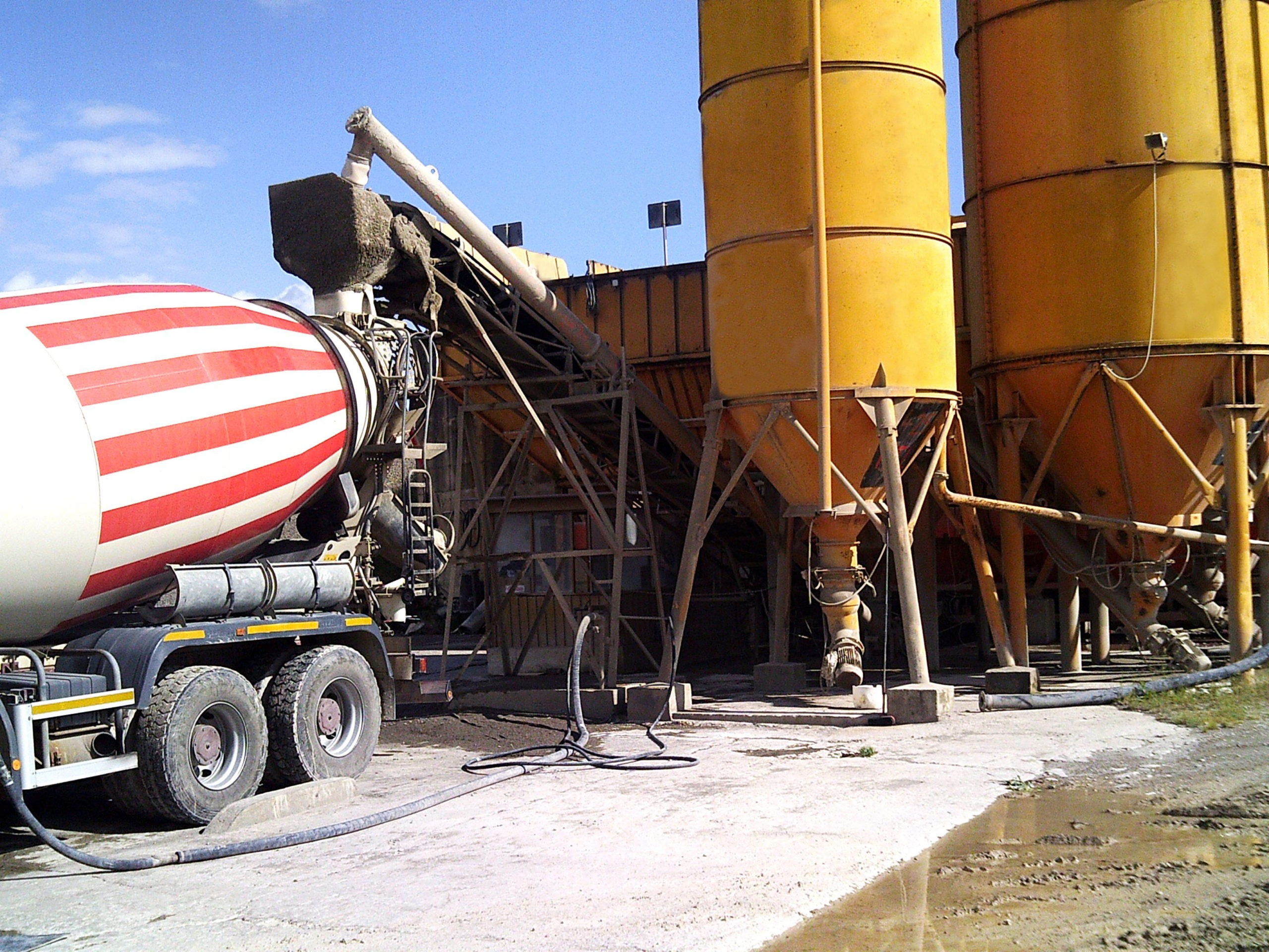 Camion betoniera vicino a silos gialli per cemento.